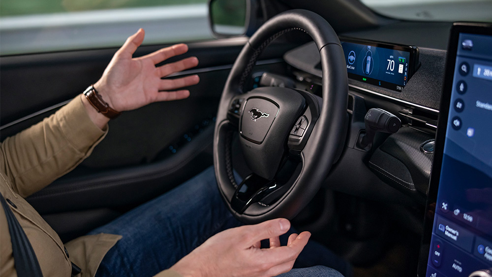 Een man zit in de Ford Mustang Mach-E met zijn handen los van het stuur, om de BlueCruise-technologie te laten zien.