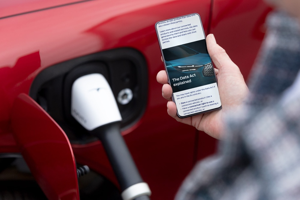 Een persoon die een uitleg over de Europese datawet op zijn telefoon leest naast een oplaadbaar elektrisch voertuig.