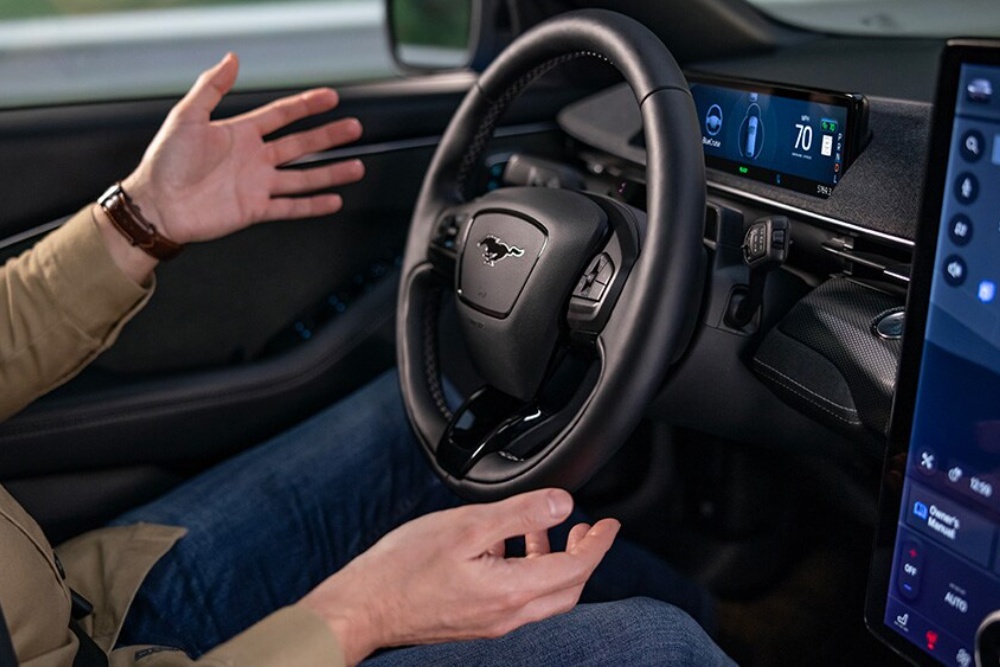 Een man zit in de Ford Mustang Mach-E met zijn handen los van het stuur, om de BlueCruise-technologie te laten zien.