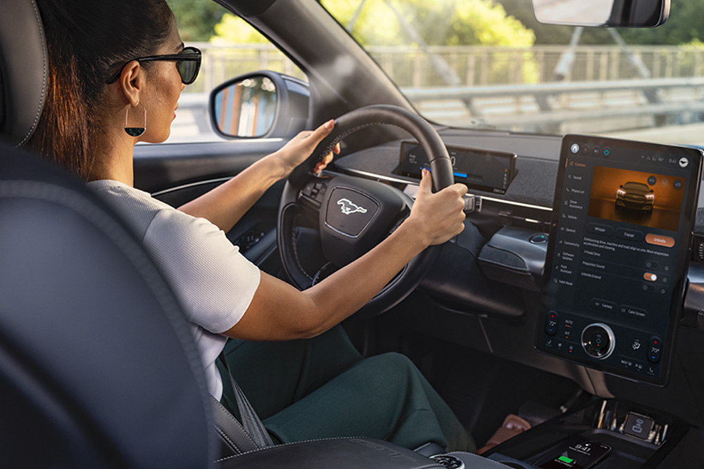 Een vrouw rijdt in de Mustang Mach-E met haar handen aan het stuur. Op het 15,5" touchscreen zie je details over de auto.