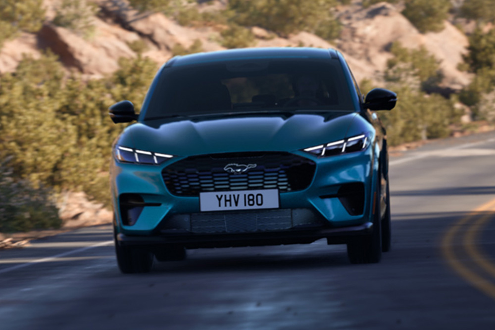 Vooraanzicht van een blauwe Ford Mustang Mach-E die op een bergweg rijdt.