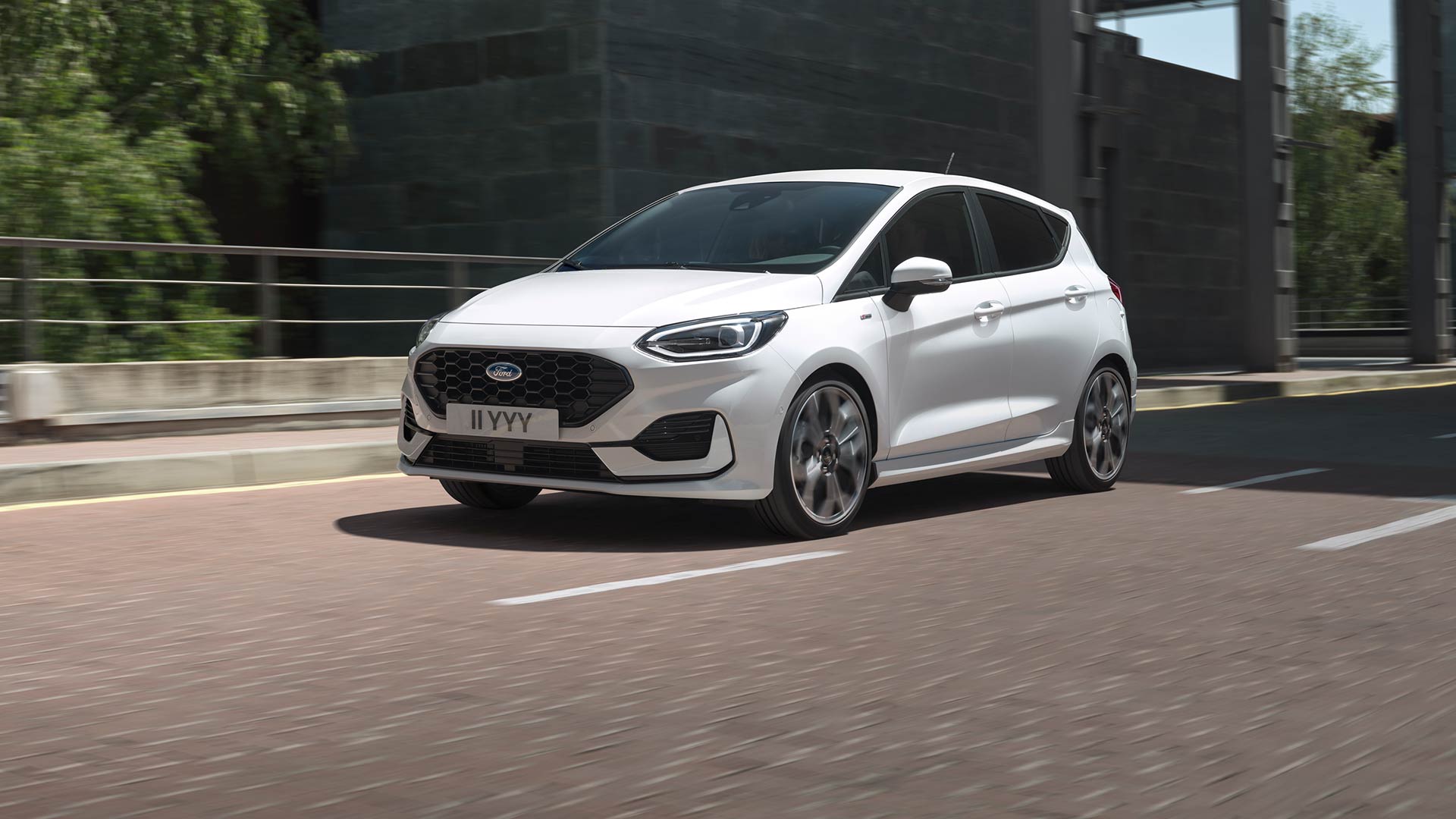 Witte Ford Fiesta rijdend op een stadsweg, met groen en gebouwen op de achtergrond.