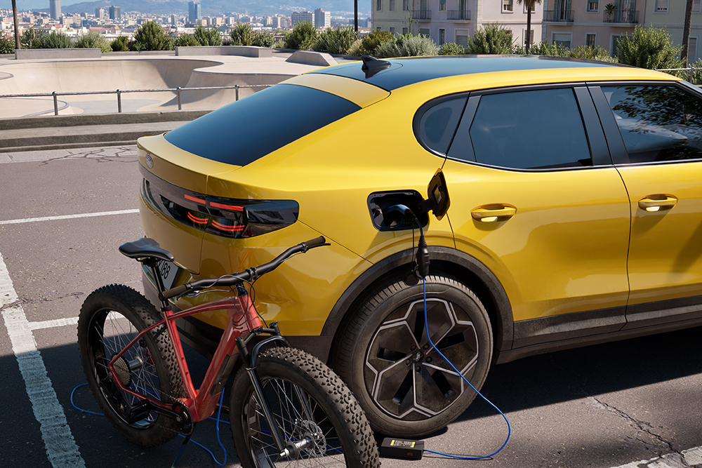 Een gele geparkeerde Ford Capr is een rode elektische fiets aan het opladen op straat