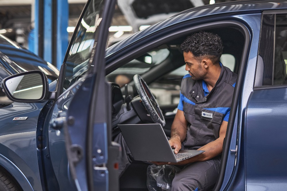 Een Ford-technicus zit op de bestuurdersstoel van een auto en voert diagnose uit op een laptop.