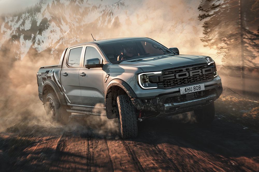 Een Ford Ranger Raptor rijdt in Baja-modus over een onverharde weg, met een berglandschap op de achtergrond.