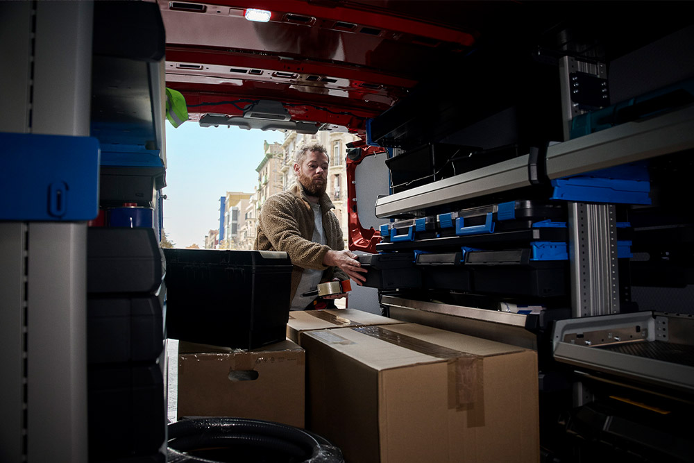 Bezorger die pakketten uitlaadt via de zijdeur van een rode Ford Transit Custom.