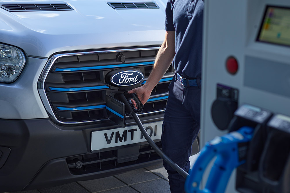 Close-up van iemand die een oplaadkabel in een zilveren Ford E-Transit elektrische bestelwagen steekt.