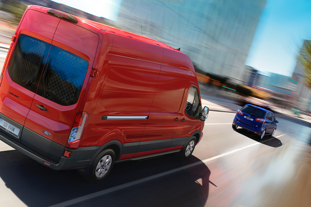 Een rode Ford Transit-bestelwagen die op een weg rijdt.