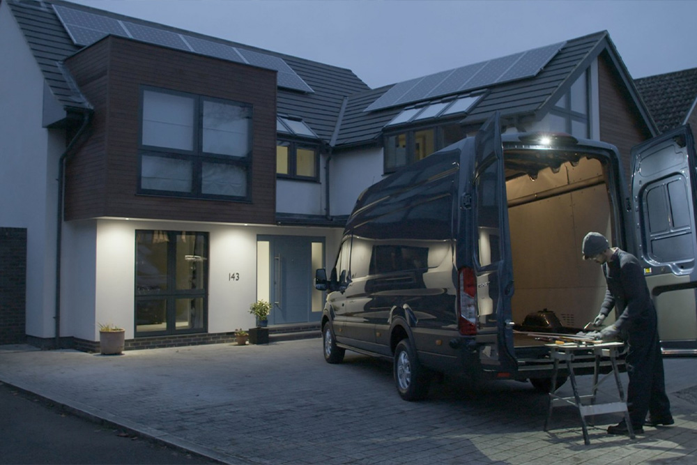 Een timmerman werkt 's nachts achter een Ford Transit-bestelwagen met open achterdeuren, verlicht door de ledspot.