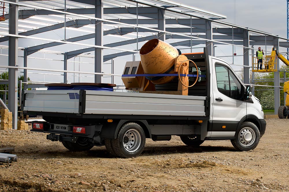 Ford Transit-chassis met cabine met een cementmixer in het laadbed geparkeerd op een bouwplaats. 