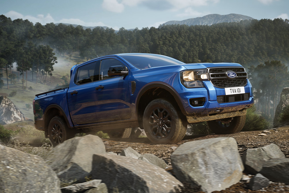 Een blauwe Ford Ranger pick-uptruck rijdt over een onverharde weg door een bos en laat een spoor van stof achter.