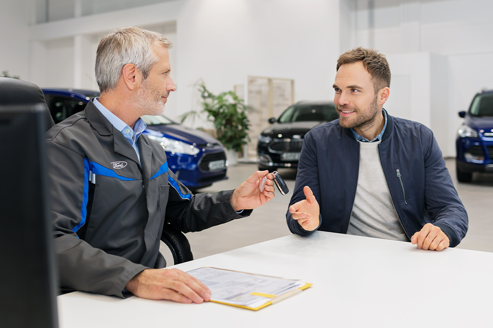 Twee mannen zitten tegenover elkaar bij een Ford dealer.