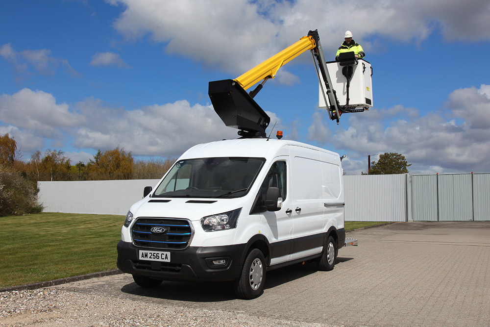 Een witte Ford Transit bestelwagen met een uitgeschoven hoogwerker, een technicus in de mand, onder een blauwe lucht.