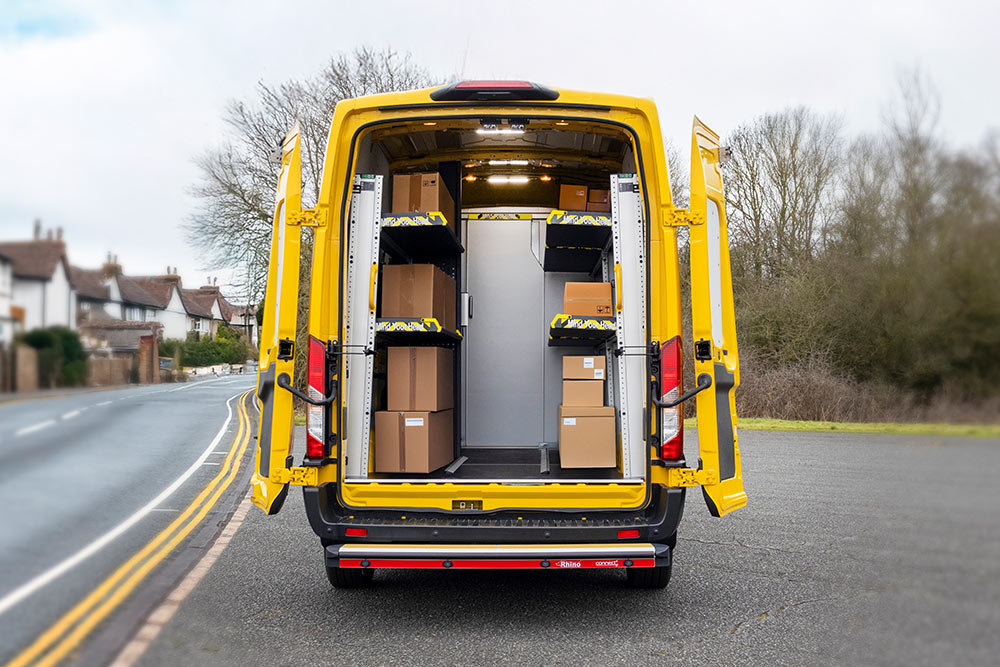 Achteraanzicht van een gele Ford Transit bestelwagen met open deuren, die een georganiseerd interieur met planken en dozen onthult.