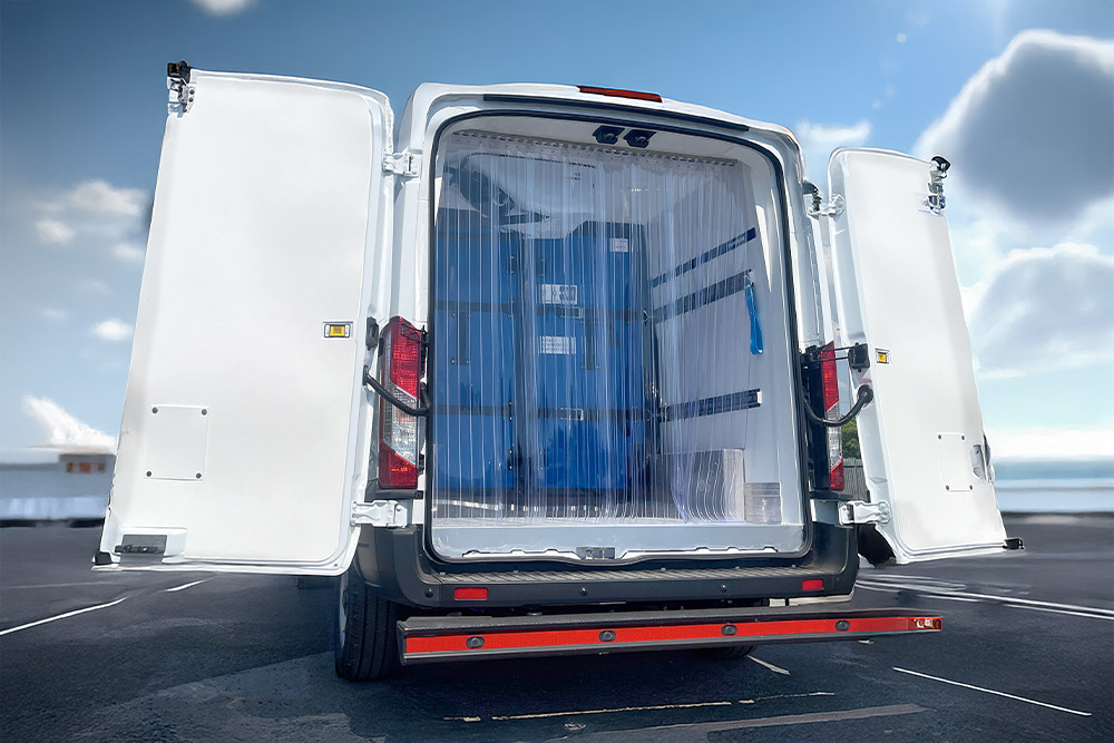 Achteraanzicht van een witte Ford Transit koelwagen met open deuren en plastic strokengordijnen.