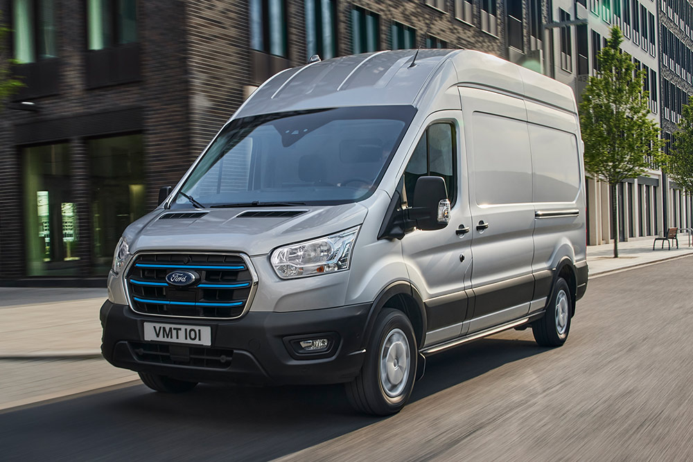 Een zilveren Ford Transit rijdt door een stedelijk landschap.