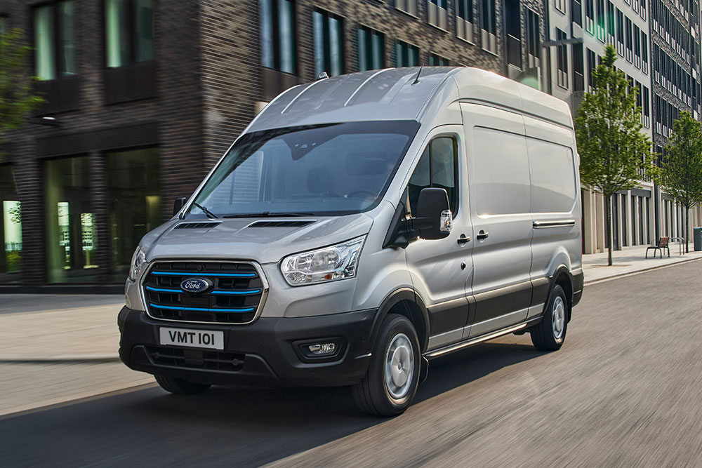 Een zilveren Ford Transit rijdt door een stedelijk landschap.