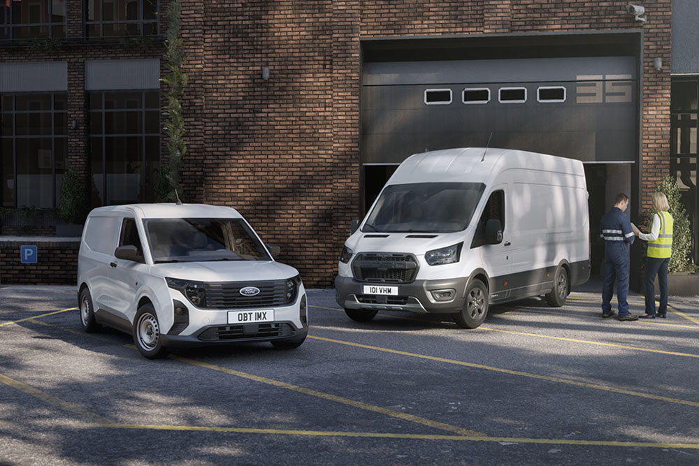 Twee witte Ford-bestelwagens staan geparkeerd voor een modern gebouw, en twee mensen staan te kletsen naast de auto's.