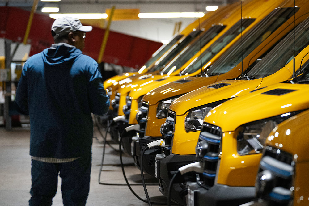  Een rij gele elektrische Ford bestelwagens wordt opgeladen, een man staat ernaast.