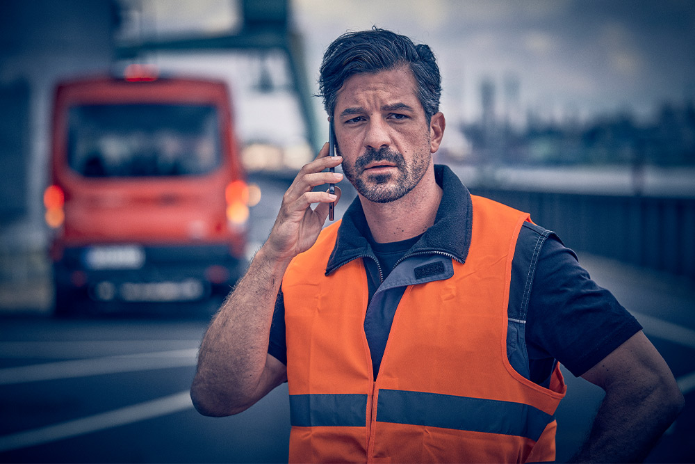  Werknemer in oranje vest belt pechhulp op een mobiel apparaat.