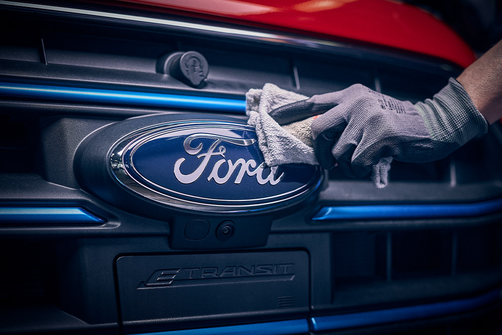  Close-up van een technicus die het Ford-logo aan de voorkant van een rode bestelwagen polijst.