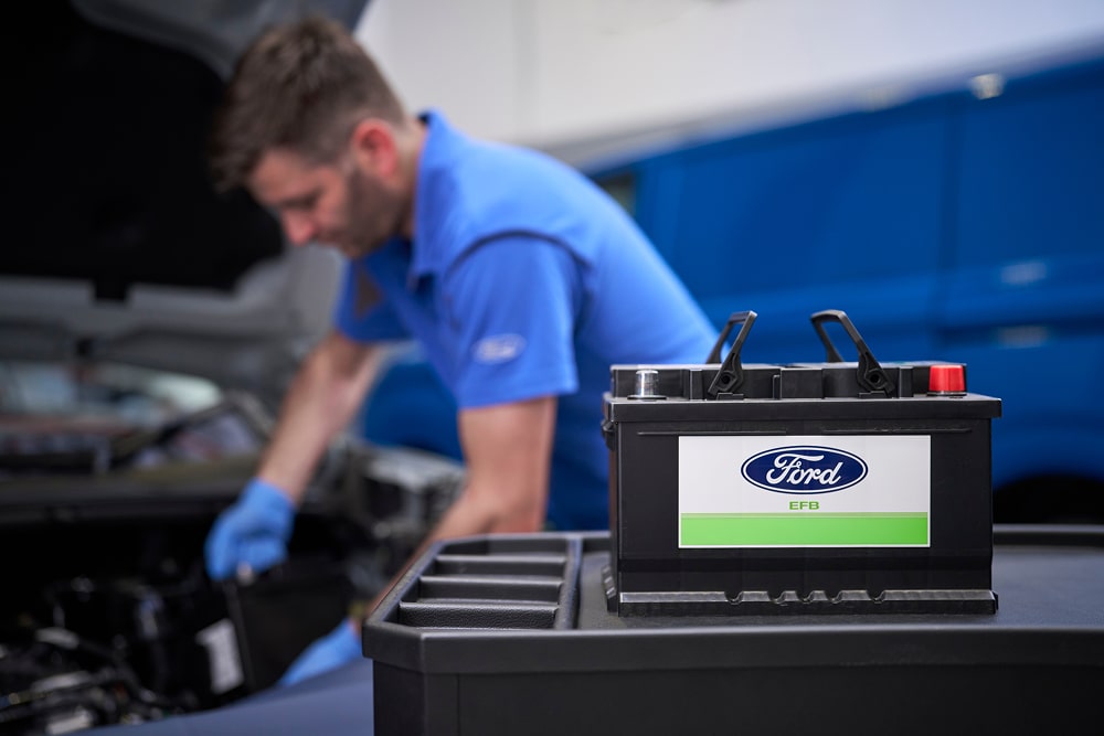 Een Ford-monteur die aan een automotor werkt, met op de voorgrond een Ford-accu.