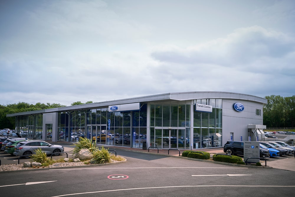 Buitenzicht van een Ford-autodealer met grote etalageruiten. Buiten staan auto's geparkeerd.